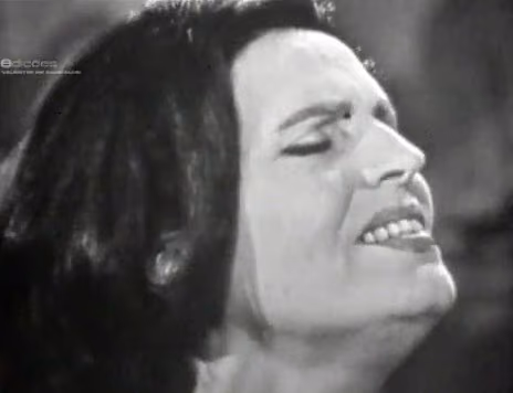 Primer plano de una cantante de Fado de Lisboa en una vieja emisión de televisión en blanco y negro, con los ojos cerrados mientras canta una frase
