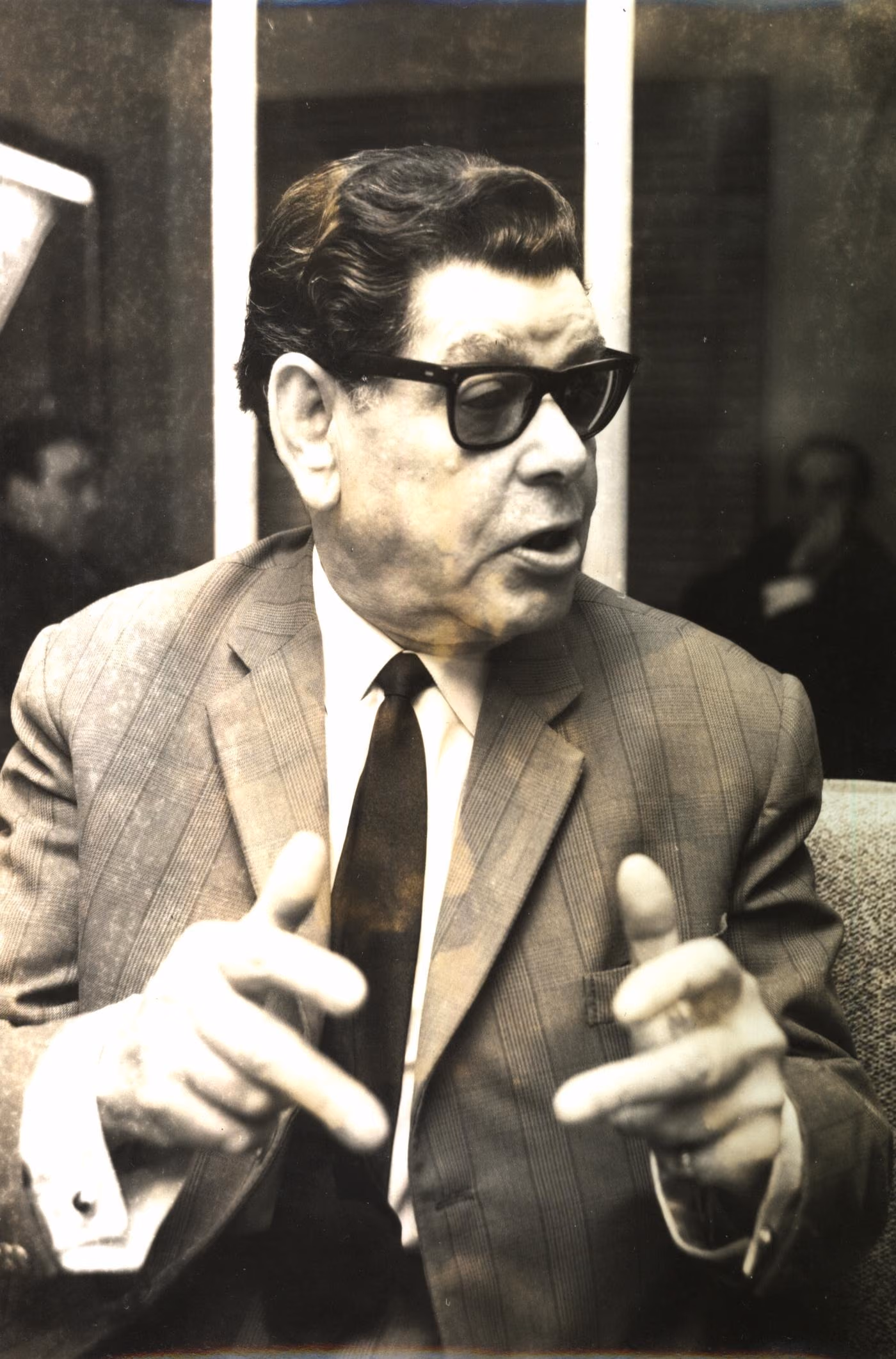 Alfredo Marceneiro, gran cantante de Fado de Lisboa, en una foto de prensa antigua: traje de rayas, gafas oscuras y las dos manos abiertas mientras habla