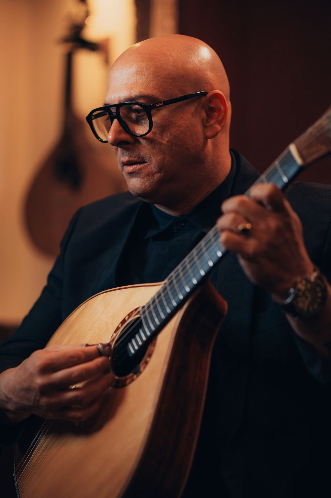 Primer plano de un guitarrista calvo, con gafas de pasta negras y gruesas, que toca la guitarra portuguesa de doce cuerdas durante un concierto de Fado en la Baixa de Lisboa