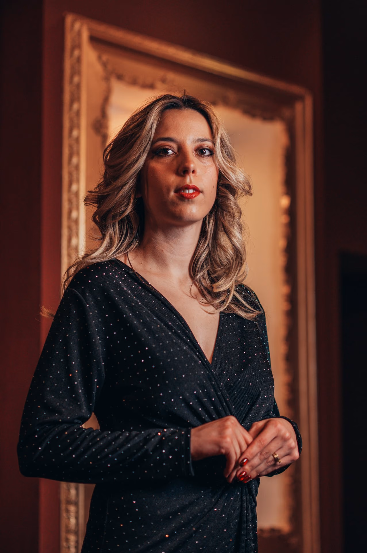 Cantante rubia de vestido negro con brillos, de pie y con las manos juntas ante el marco dorado de la pared granate, en nuestra sala de Fado de la Baixa, en Lisboa