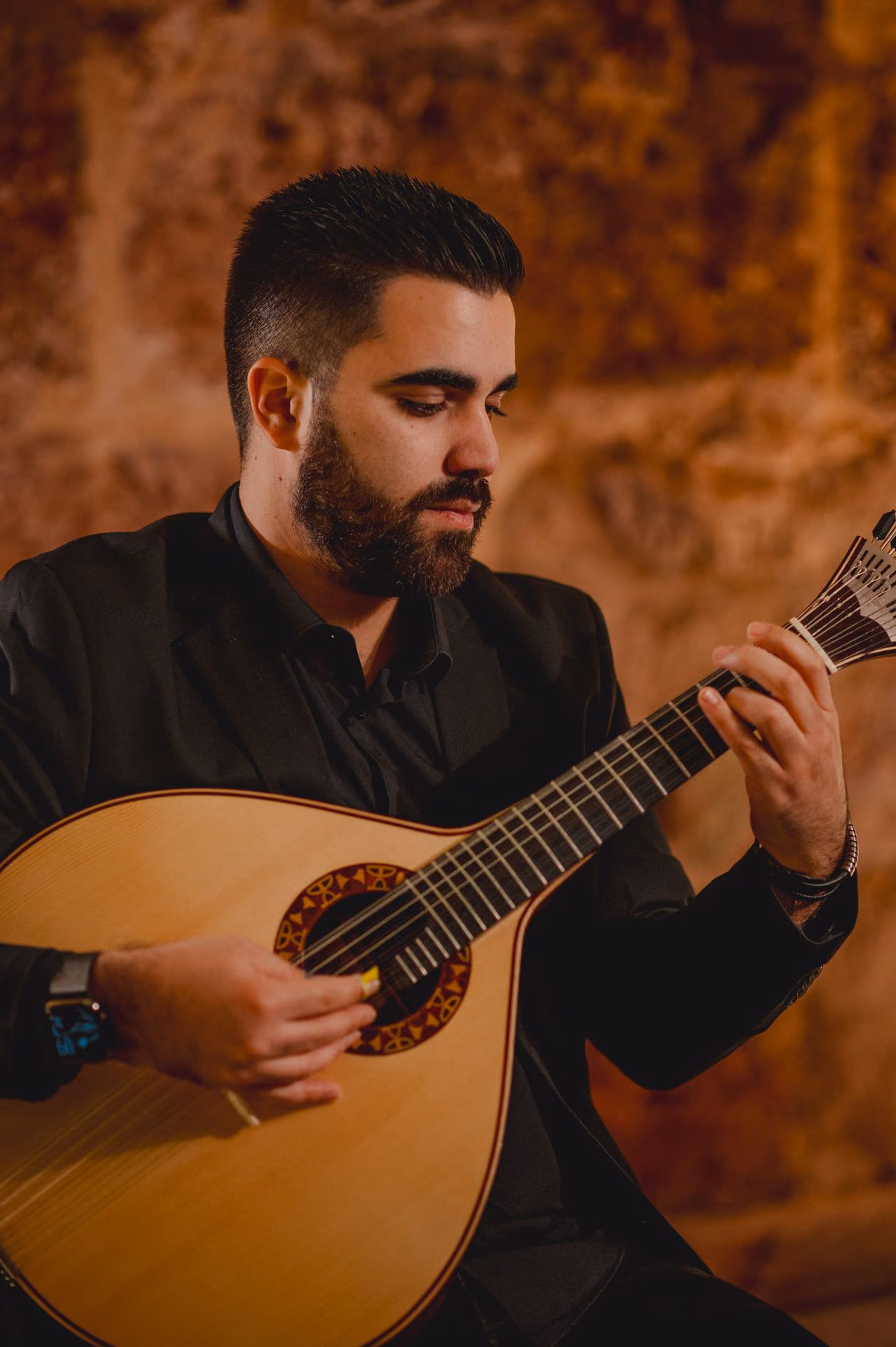 Guitarrista con barba que toca la guitarra portuguesa ante los muros de piedra de nuestra sala de Fado de la Sé, en Lisboa