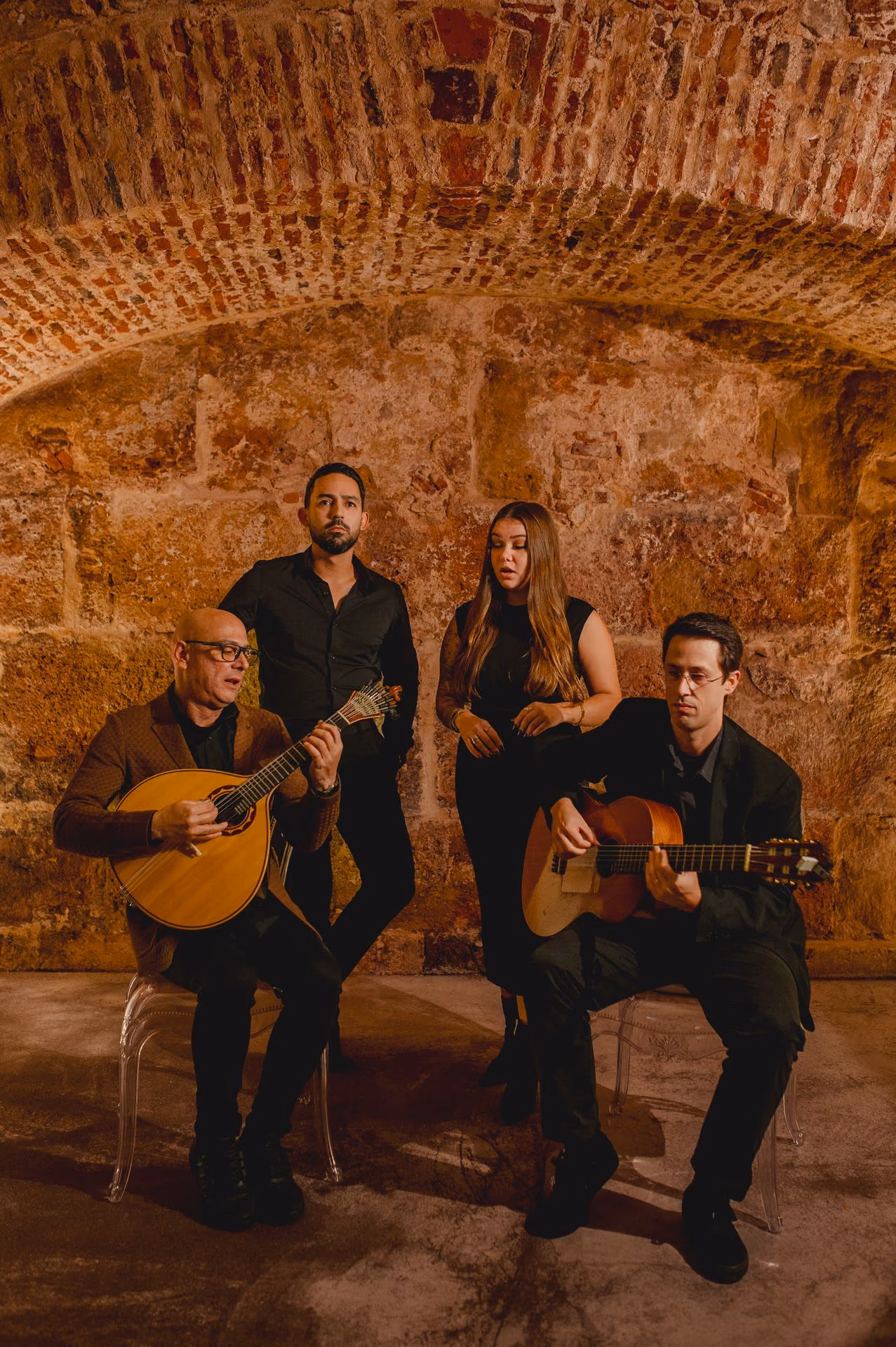 Cuatro músicos de Fado, dos cantantes y dos guitarristas, unos sentados y otros de pie, bajo el arco de piedra de la sala de la Sé, en Lisboa