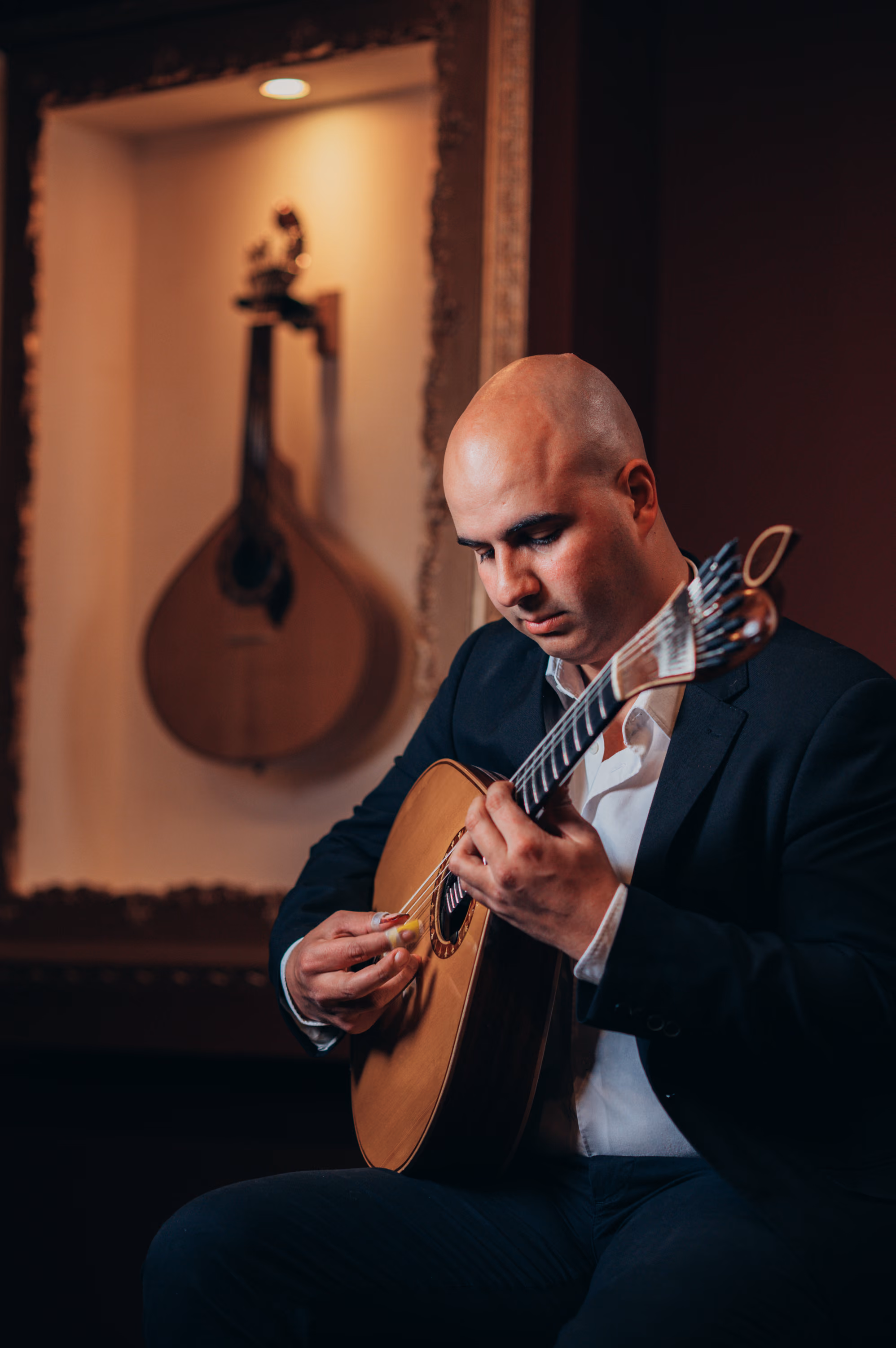 Un guitarrista calvo con la mirada en la guitarra portuguesa, la guitarra del Fado; al fondo, otra cuelga en una hornacina iluminada de la sala de la Baixa, en Lisboa