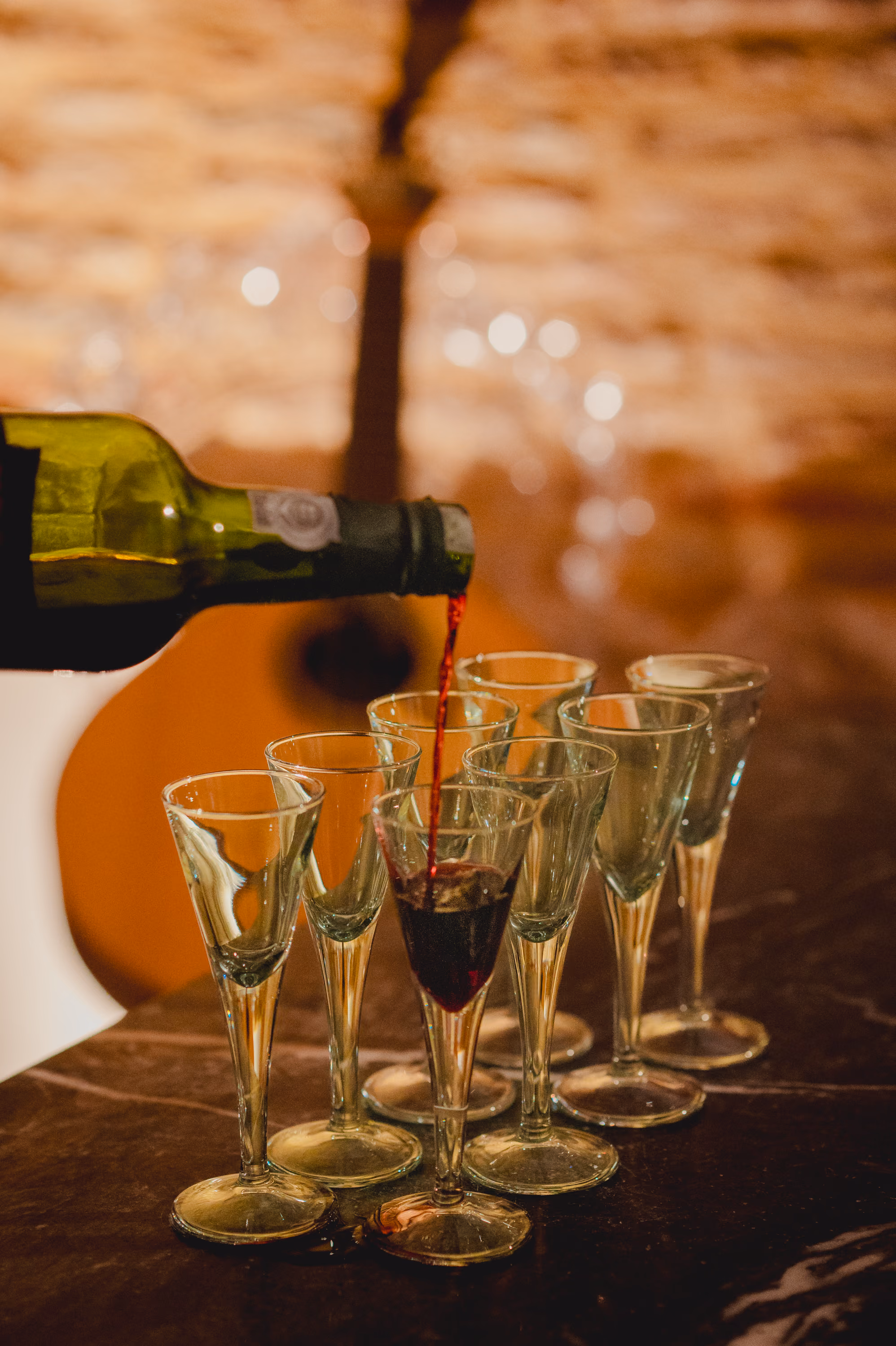 Se sirve vino tinto portugués en una hilera de copitas antes de un concierto de Fado en Lisboa; al fondo, una guitarra desenfocada
