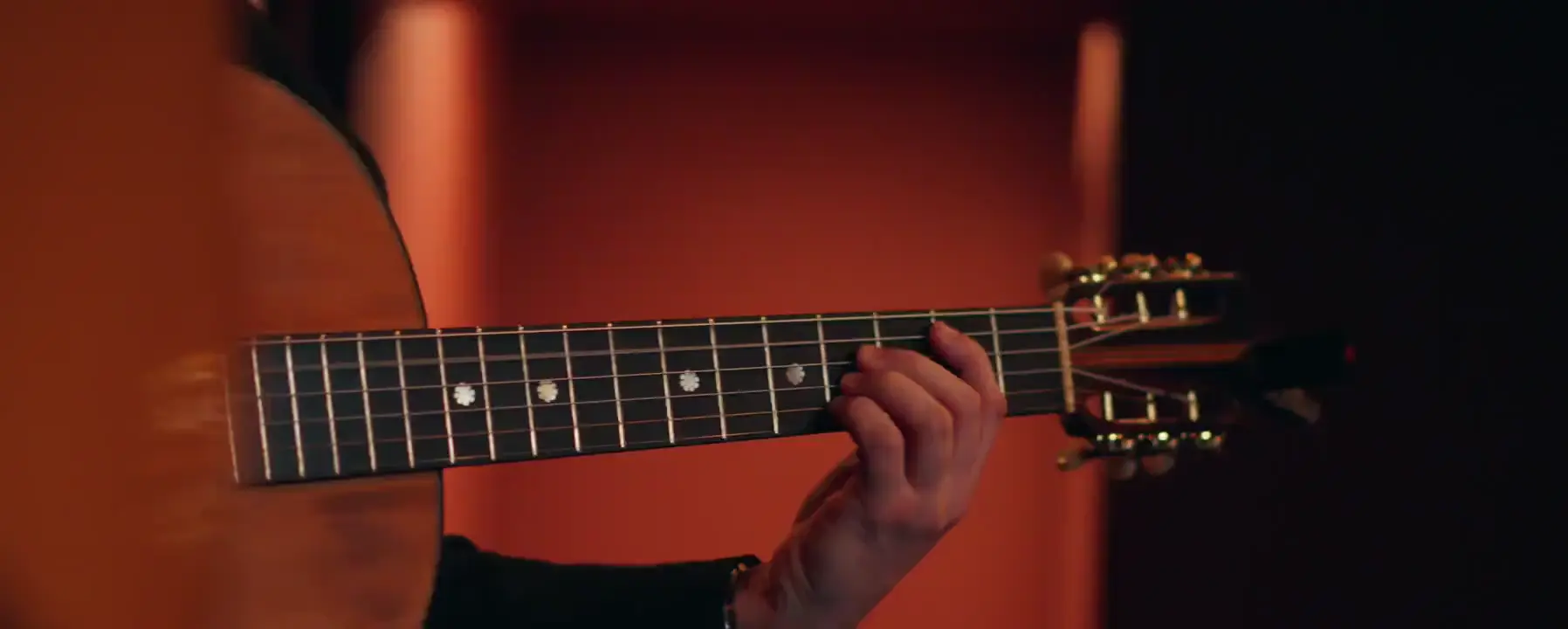 Una mano en el mástil de una guitarra clásica, ante una pared roja de la sala de la Baixa, en Lisboa: primer fotograma de una película sobre el Fado